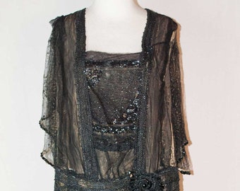May include: A vintage black and gold dress on a mannequin. The dress features a square neckline, beaded accents, and a decorative floral belt. The skirt has vertical stripes, and the sleeves are short and sheer.