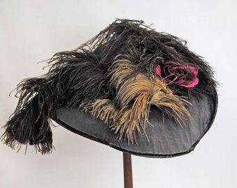 May include: A vintage black hat with a wide brim, adorned with black and tan feathers and a deep pink rose. The hat is displayed on a wooden hat stand, showcasing its elegant design and craftsmanship.