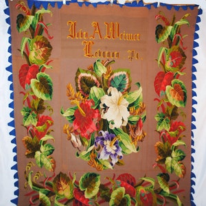 以下が含まれることがあります： 茶色の織物で、花の模様と「John A. Weimer Lebanon Pa.」の文字が入っています。中央の花の配置は、赤、白、紫の花と緑の葉が特徴です。青色のスカラップのボーダーが作品を縁取っています。