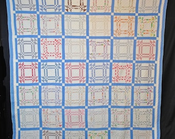 Puede incluir: Un edredón hecho a mano con un patrón repetido de cuadrados. Cada cuadrado presenta un diseño central en varios colores, incluyendo rojo, azul y marrón, sobre un fondo blanco. El edredón está bordeado con un marco azul claro.