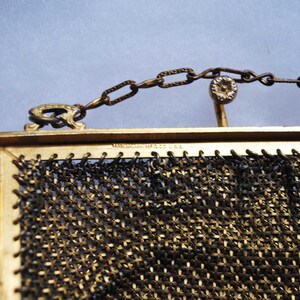 May include: Close-up of a vintage gold-toned mesh purse with a chain handle. The purse has a rectangular frame and a delicate, woven mesh design. The chain and frame show signs of age, adding to its antique charm. The text "MANHATTAN MFG CO. U.S.A." is visible.