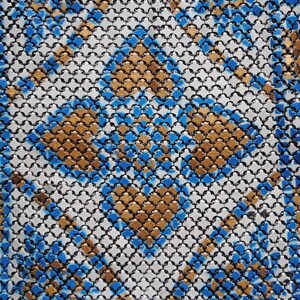 May include: Close-up of a patterned textile with a repeating geometric design. The pattern features a grid of small, interconnected shapes in black, white, gold, and blue. The gold and blue elements create a diamond-like pattern.