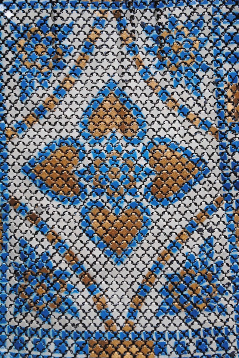 May include: Close-up of a patterned textile with a repeating geometric design. The pattern features a grid of small, interconnected shapes in black, white, gold, and blue. The gold and blue elements create a diamond-like pattern.