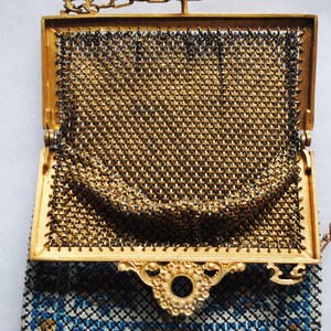 May include: An open, antique gold-toned metal mesh purse with a decorative frame and chain handle. The purse features a detailed, ornate clasp and a blue and white patterned lining visible at the bottom.