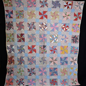May include: A handmade quilt with a pinwheel pattern. The quilt features squares of various patterned fabrics in shades of blue, red, pink, and beige. The pinwheel blocks are set against a light blue floral background, creating a vintage aesthetic.