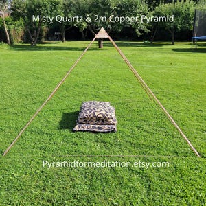 May include: A large copper pyramid frame structure with a small apex piece, positioned over a stack of three black and beige patterned cushions. The text Misty Quartz & 2m Copper Pyramid and Pyramidformeditation.etsy.com is visible on the image.
