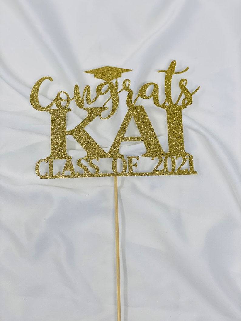 May include: Gold glitter graduation cake topper with the text "Congrats Kai Class of 2021".