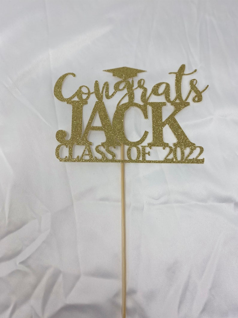 May include: Gold glitter graduation cake topper with the text "Congrats Jack Class of 2022".
