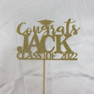 May include: Gold glitter graduation cake topper with the text "Congrats Jack Class of 2022".