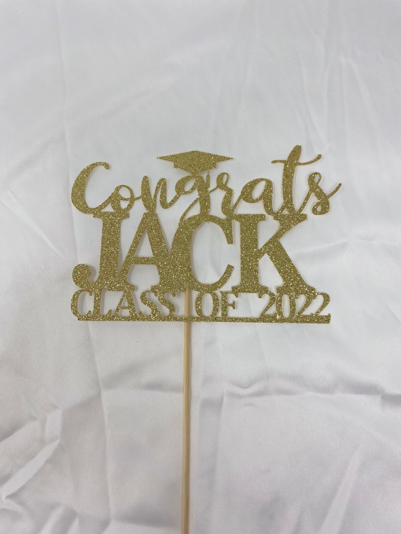May include: Gold glitter graduation cake topper with the text "Congrats Jack Class of 2022".