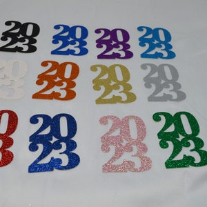 May include: Assortment of 2023 graduation year cutouts in various glitter colors, including black, blue, purple, silver, gold, red, pink, and green.