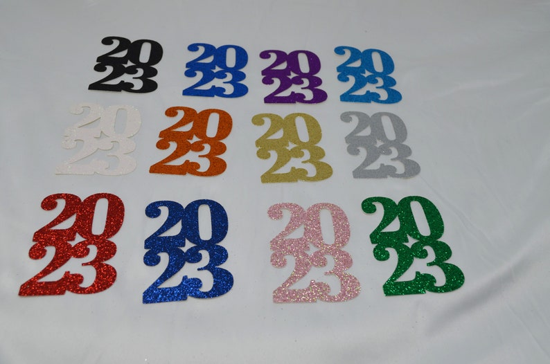 May include: Assortment of 2023 graduation year cutouts in various glitter colors, including black, blue, purple, silver, gold, red, pink, and green.