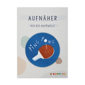 Può includere: Un toppa termoadesiva blu e arancione con le parole "PING PONG" e un'immagine di un tavolo da ping pong e una palla. La toppa è realizzata in cotone biologico ed è etichettata "AUFNÄHER AUS BIO-BAUMWOLLE".