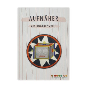Könnte beinhalten: Ein farbenfroher Bügelaufkleber mit einem Cartoon-Roboter mit gelbem, blauem und rotem Körper. Der Roboter ist von einem weißen Sternenausbruch auf schwarzem Hintergrund mit orangefarbenem Rand umgeben. Der Text "AUFNÄHER AUS BIO-BAUMWOLLE" ist auf der Karte gedruckt.