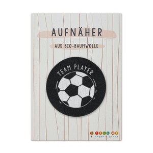 Könnte beinhalten: Schwarz-weißes Bügelbild mit einem Fußball und dem Text "Team Player" in Weiß. Das Bügelbild befindet sich auf einem weißen Hintergrund mit dem Text "Aufnäher aus Bio-Baumwolle" in Schwarz.