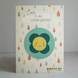 Könnte beinhalten: Eine hellblaue Karte mit einer gelben Sonne mit einem grünen Blumenmuster und dem Text "Loch in der Lieblingshose?" Die Karte hat eine weiße Wolke mit Regentropfen in verschiedenen Farben.