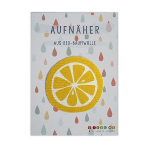 Könnte beinhalten: Ein gelber Zitronenscheiben-Aufnäher mit dem Text "AUFNÄHER AUS BIO-BAUMWOLLE" und dem Logo "TELL ME organic goods".