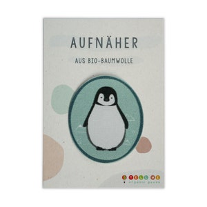 Può includere: Un cerotto rotondo blu e bianco da stirare con un pinguino dei cartoni animati su uno sfondo blu chiaro. Il cerotto dice "AUFNÄHER AUS BIO-BAUMWOLLE" in testo nero. Il cerotto è del marchio "TELL ME organic goods".