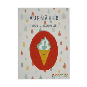 Puede incluir: Un parche de tela rojo con un diseño de cono de helado sonriente. El helado es verde y blanco y el cono es amarillo. El parche dice "AUFNÄHER AUS BIO-BAUMWOLLE" y "TELL ME organic goods".