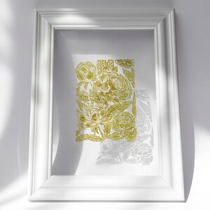 May include: White framed art print featuring a gold floral design. The artwork showcases a detailed pattern of flowers and leaves, set against a white background. The frame is a simple, clean design.