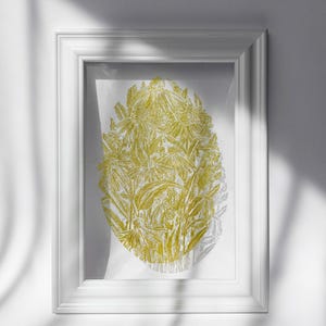 May include: A framed print featuring a gold-colored floral design. The artwork is an oval composition of detailed flowers and leaves, set against a white background. The print is encased in a white, rectangular frame.