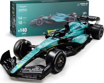 May include: A model kit of an Aston Martin Formula 1 car in teal and black. The car has sponsor logos and the number 18. The box shows the car and details like "14+," "140+ parts," and "Scale 1:18."