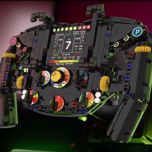 May include: Black racing wheel with a digital display showing numbers and data. The wheel has multiple buttons, dials, and yellow gears. The text "Racing wheels" is visible on the display.