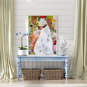 Op de afbeelding: Een lichtblauwe consoletafel met twee rieten manden eronder. Een ingelijst abstract schilderij van een witte figuur met een kleurrijke achtergrond hangt boven de tafel. Een gepotte orchidee en een wit koraalbeeld staan op de tafel.