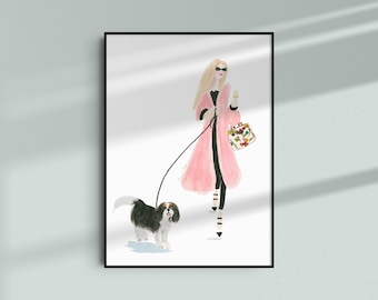 May include: A woman in a pink coat walks a black and white Cavalier King Charles Spaniel on a leash. She is carrying a floral patterned handbag.