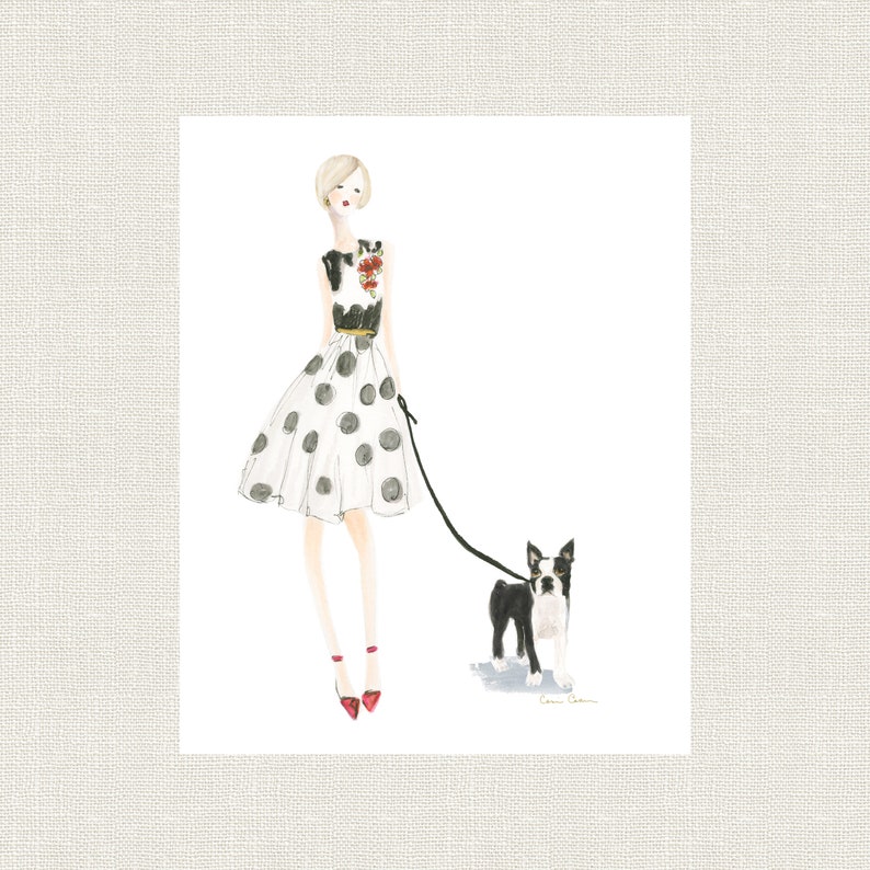 Op de afbeelding: Een vrouw in een witte jurk met zwarte stippen loopt met een zwart-witte Boston Terrier aan de lijn. Ze draagt rode schoenen en een zwart topje met een bloemenprint.
