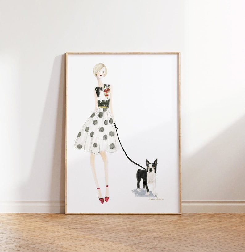 Op de afbeelding: Een aquarelillustratie van een vrouw in een witte polkadotrok en een zwart topje die een Boston Terrier aan de lijn uitlaat. De vrouw draagt rode schoenen en heeft blond haar. De achtergrond is wit.