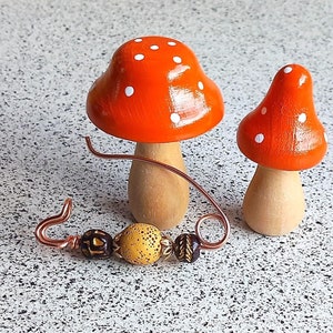Può includere: Due figurine di fungo in legno con cime rosse e bianche a pois. Un filo di rame con perline marroni e gialle è in primo piano.