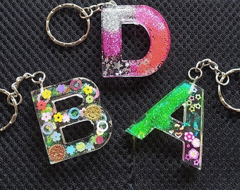 May include: Three resin letter keychains with glitter and embellishments. The letters are "A", "B", and "D".