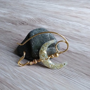 May include: A gold wire crescent moon charm with a white glitter finish. The charm is attached to a gold wire loop and has a gold bead accent.