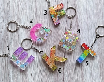 May include: Six resin letter keychains with different colors and designs. The letters are E, G, F, B, T, and K. Each keychain has a silver metal ring and chain.