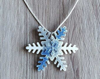 Op de afbeelding: Een witte touwtjesketting met een blauwe en witte glitter sneeuwvlok hanger.
