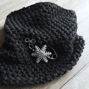 May include: A black crocheted scarf with a white snowflake pin attached.