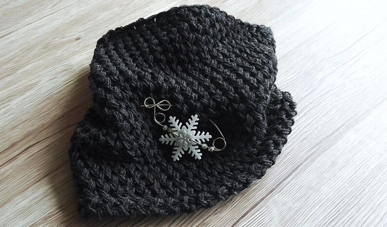 May include: A black crocheted scarf with a white snowflake pin attached.