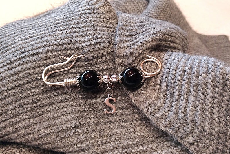 May include: A silver brooch with two black beads and a silver charm with the letter 'S'.