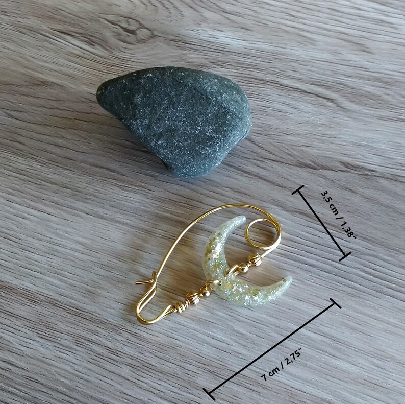 May include: Gold tone shawl pin with a crescent moon design. The moon is made of clear resin with gold glitter. The pin measures 3.5 inches long and 2.75 inches wide.