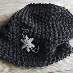 May include: A dark gray knitted hat with a white snowflake pin attached.