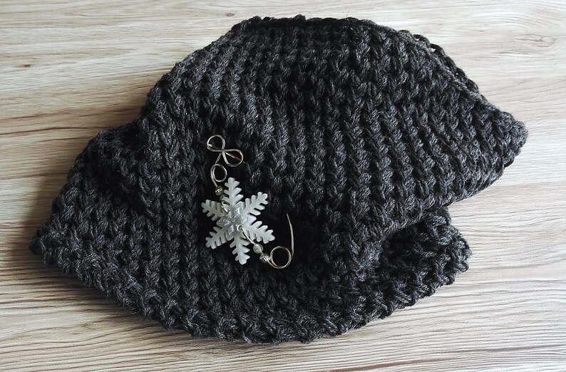 May include: A dark gray knitted hat with a white snowflake pin attached.