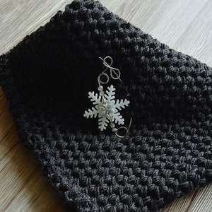 May include: A black crocheted scarf with a white snowflake charm attached to it.