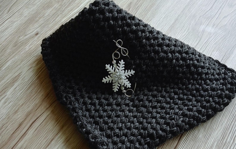 May include: A black crocheted scarf with a white snowflake charm attached to it.