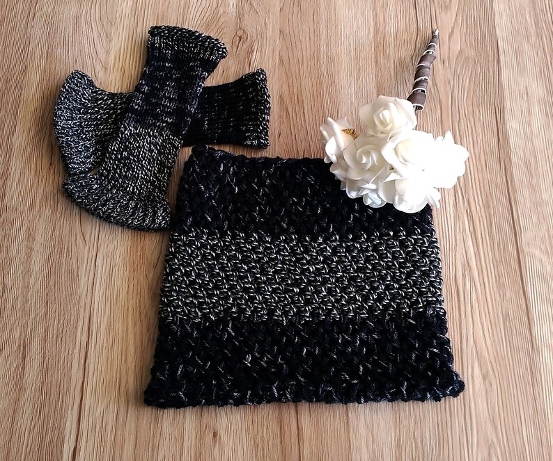 May include: Black and silver crocheted cowl with a striped pattern. The cowl is folded and displayed on a wooden surface.