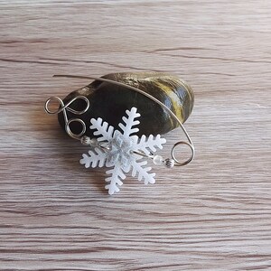 May include: A white snowflake charm with silver wire and beads, on a wooden surface.