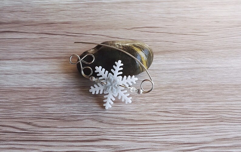 May include: A white snowflake charm with silver wire and beads, on a wooden surface.