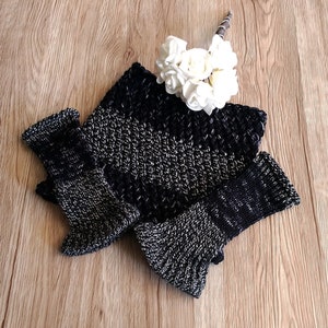 May include: A black and silver knitted fingerless glove set with a textured pattern. The gloves are folded together on a wooden surface.