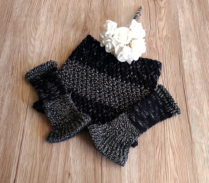 May include: A black and silver knitted fingerless glove set with a textured pattern. The gloves are folded together on a wooden surface.