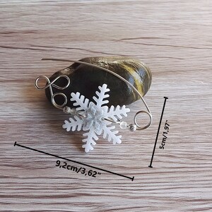May include: A silver wire snowflake ornament with a white snowflake charm, measuring 5 cm by 9.2 cm.